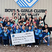 Group of children and adults raising hands up outside of a Boys & Girls Club building and holding a large check for $100,000