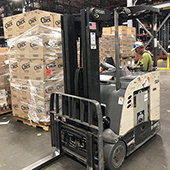 Man driving forklift next to large boxes in warehouse