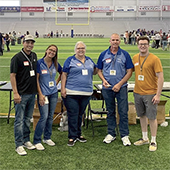Five people standing in front of table on indoor football field.