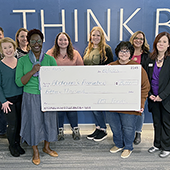 Group of people smiling in office and holding a large check for $15,000 to the Alzheimer's Association