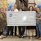 Group of people in warehouse holding large check for $50,000