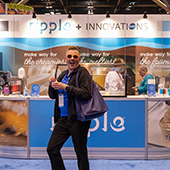 Person posing in front of trade show booth with big smile and sunglasses