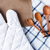 Overhead shot of a white oven mitt, blue and white striped towel, and three wooden measuring spoons
