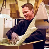 Male warehouse employee packing a box with plastic packing material