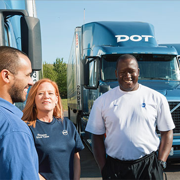Two male and one female Dot Transportation truck drivers in front of two Dot blue trucks