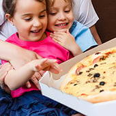 Two children smiling excitedly at a pizza